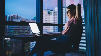 Femme travaillant tard sur un ordinateur portable dans un bureau moderne avec vue sur la ville.